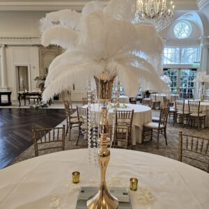 Gold centerpiece with white ostrich feathers on a glass mirror base with votive candles at the Park Chateau in New Jersey done by PMT Party Services Group