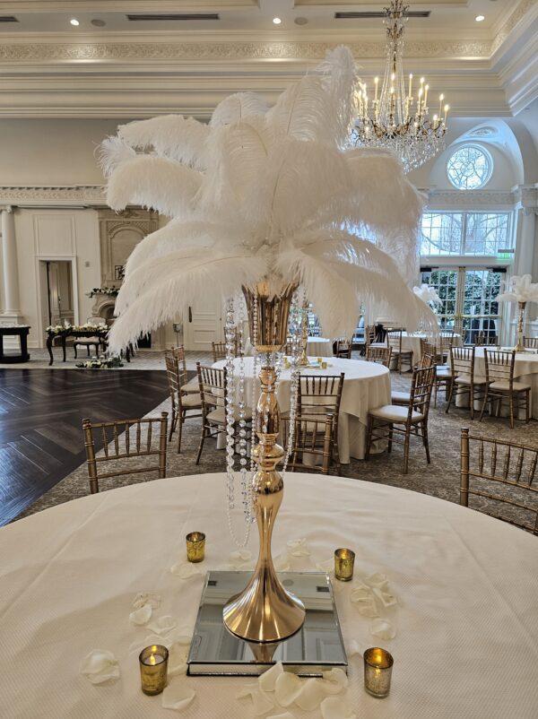 Gold centerpiece with white ostrich feathers on a glass mirror base with votive candles at the Park Chateau in New Jersey done by PMT Party Services Group