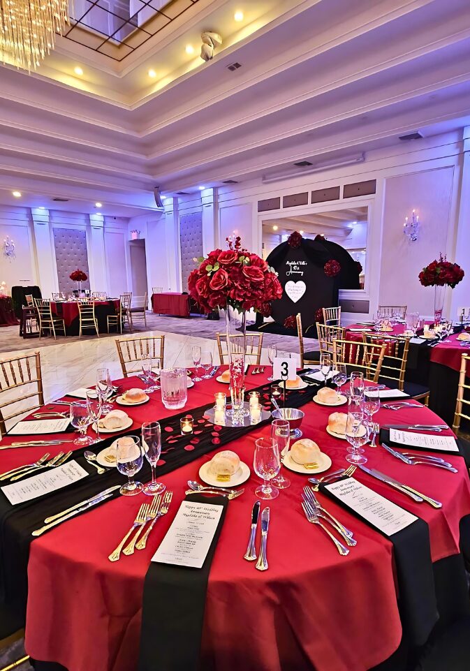 Migdalia's Anniversary: Table setup, chair setup, glass cylinder centerpieces, burgundy table skirts, glass trumpet vase with red roses arrangement, 7.2ft arch with black fabric and custom white vinyl with red roses arrangements done by PMT Party Services Group at the Grand Plaza in Staten Island, New York