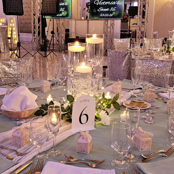 3 glass cylinders with floating candles, filled with clear water gel beads and decorated with acrylic diamonds, pearls, and floating candles, placed on a 12in mirror charger, surrounded by white/ivory rose garland and fairy lights, decorations, candle ceremony, Queen Tiffany throne, table setup, centerpieces, gold pedals for Victoria's Sweet 16 in Staten Island, New York at the Grand Plaza done by PMT Party Services Group