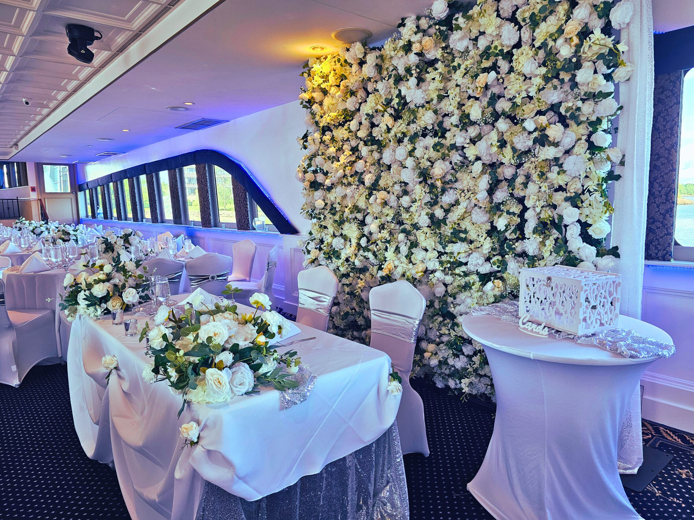 Jackie's Atlantis Yacht Event detailing wedding decor with an elaborate white rose flower wall and centerpieces. Yacht sailed from Samford, CT to Brooklyn, NY. All decorations done by PMT Party Services Group on the Atlantis Yacht.